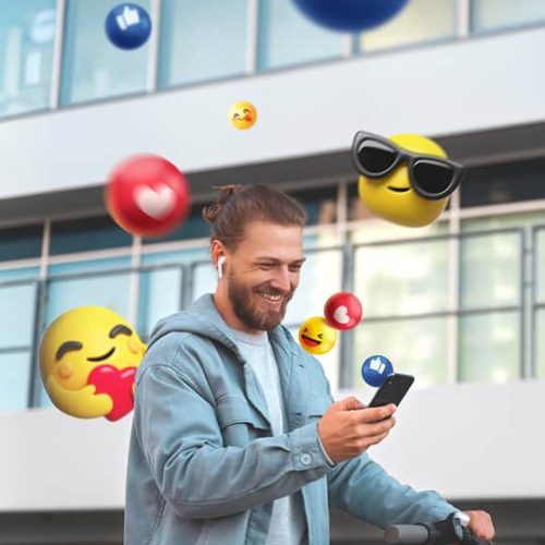 A man in a light jacket looks at his phone and smiles, surrounded by floating social media and emoji icons against a modern building background.